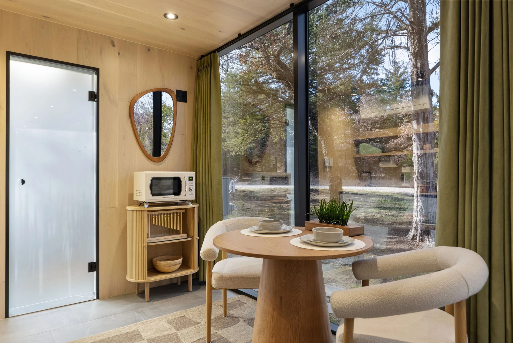 ÖÖD Extended interior with a dining table, timber finishes, and full-height mirror-glass window wall.