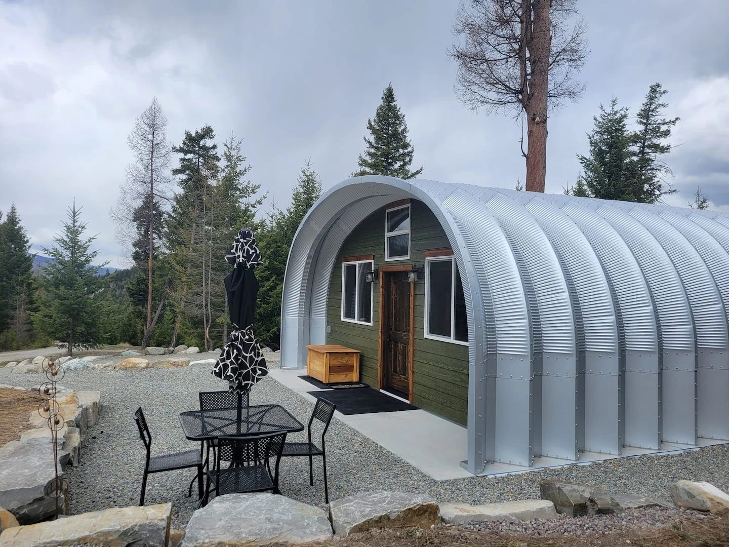 Steel arch cabin with a recessed dark end wall in a Montana forest.