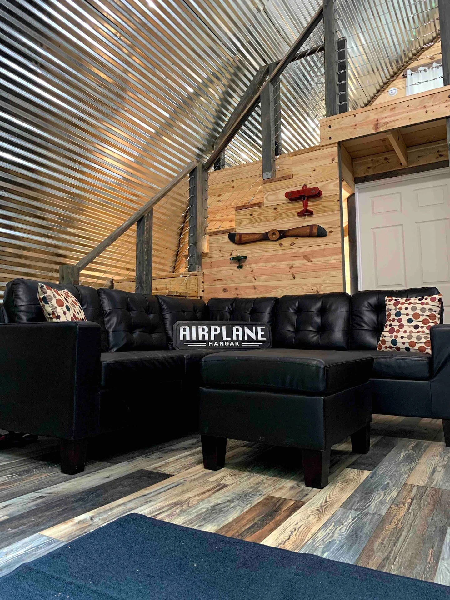Black sofa below a loft and corrugated steel arch inside Hangar 22.