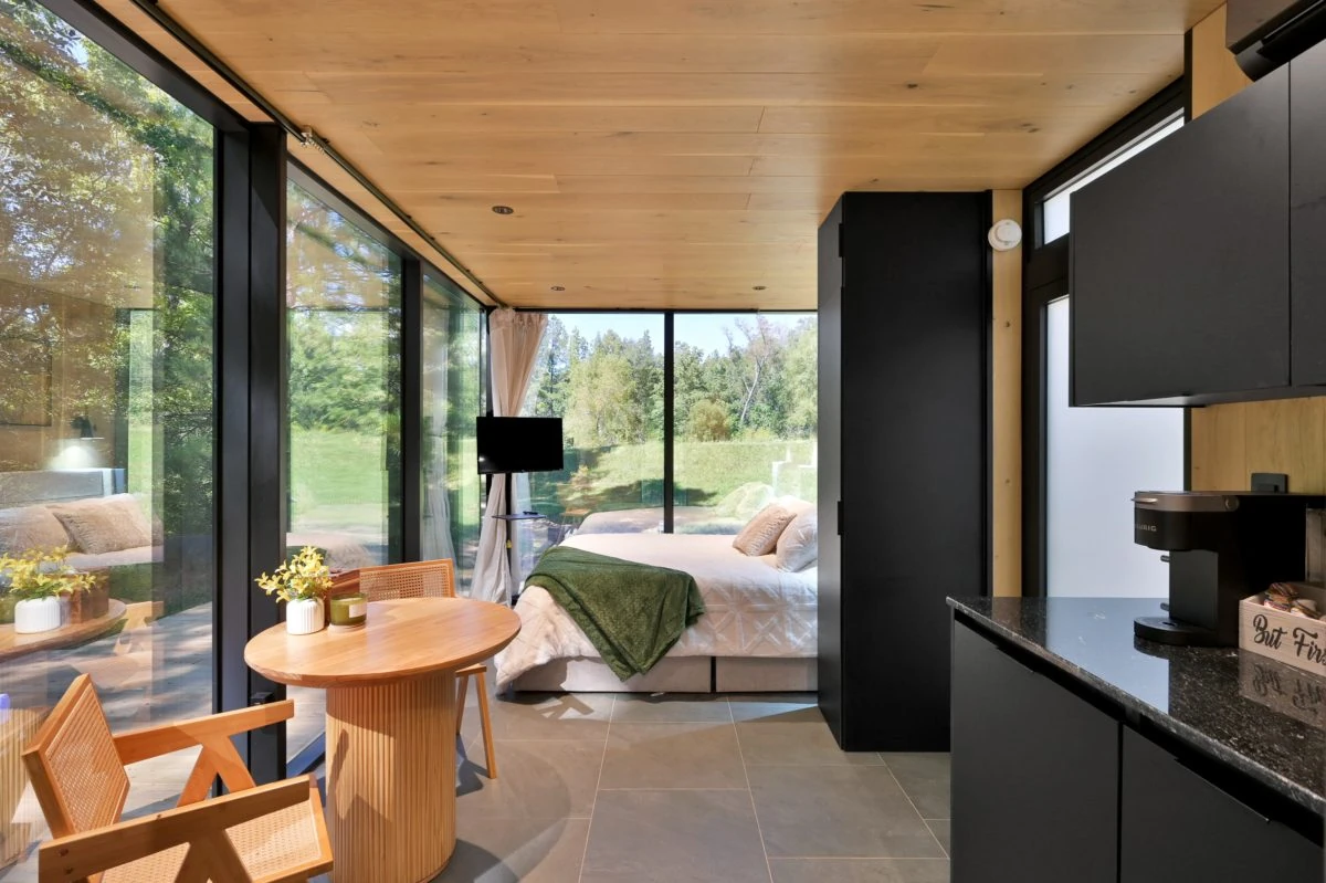 Bed, small table and kitchenette beside full height glass at Cameron Ranch.