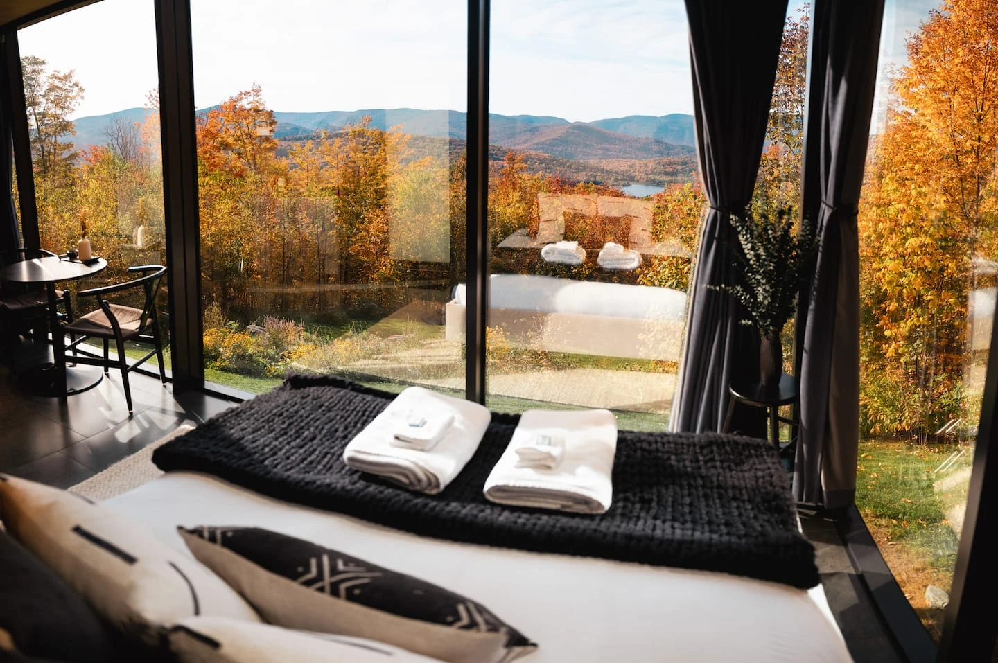 Bed beside full height windows looking over Vermont mountains and autumn trees.
