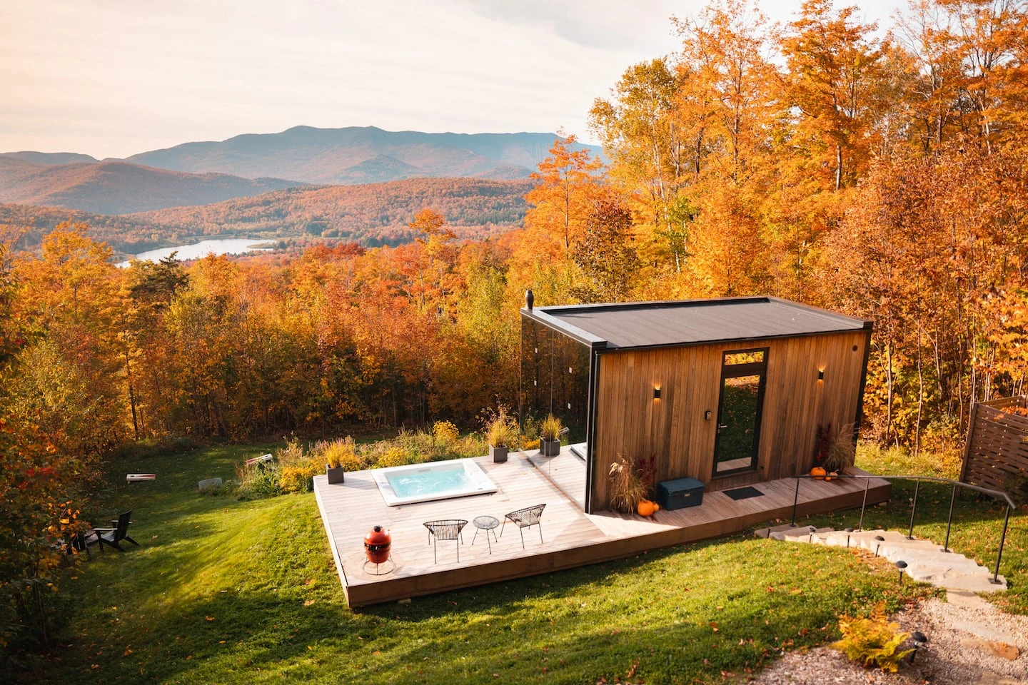 Wood rear wall of a small house beside a hot tub deck overlooking autumn trees.